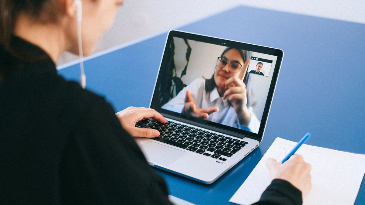 Woman participating in a virtual meeting, taking notes during a video conference on a laptop.