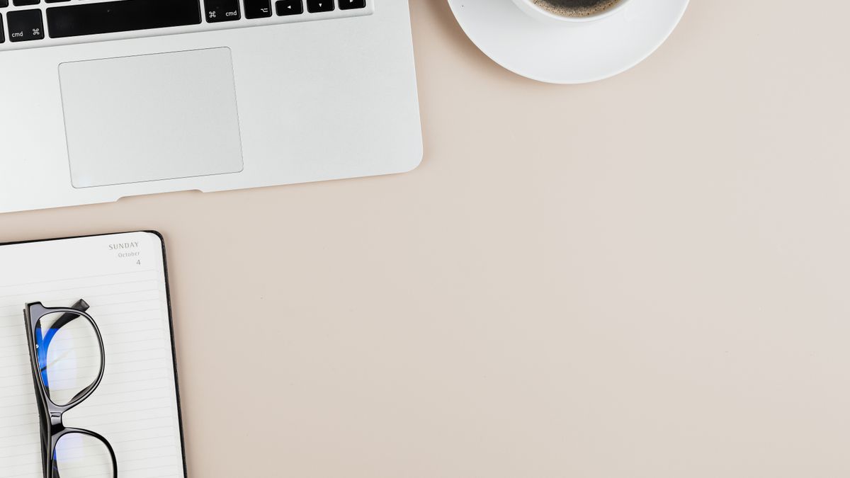 A tidy office desk setup with a laptop, notebook, coffee, and eyeglasses